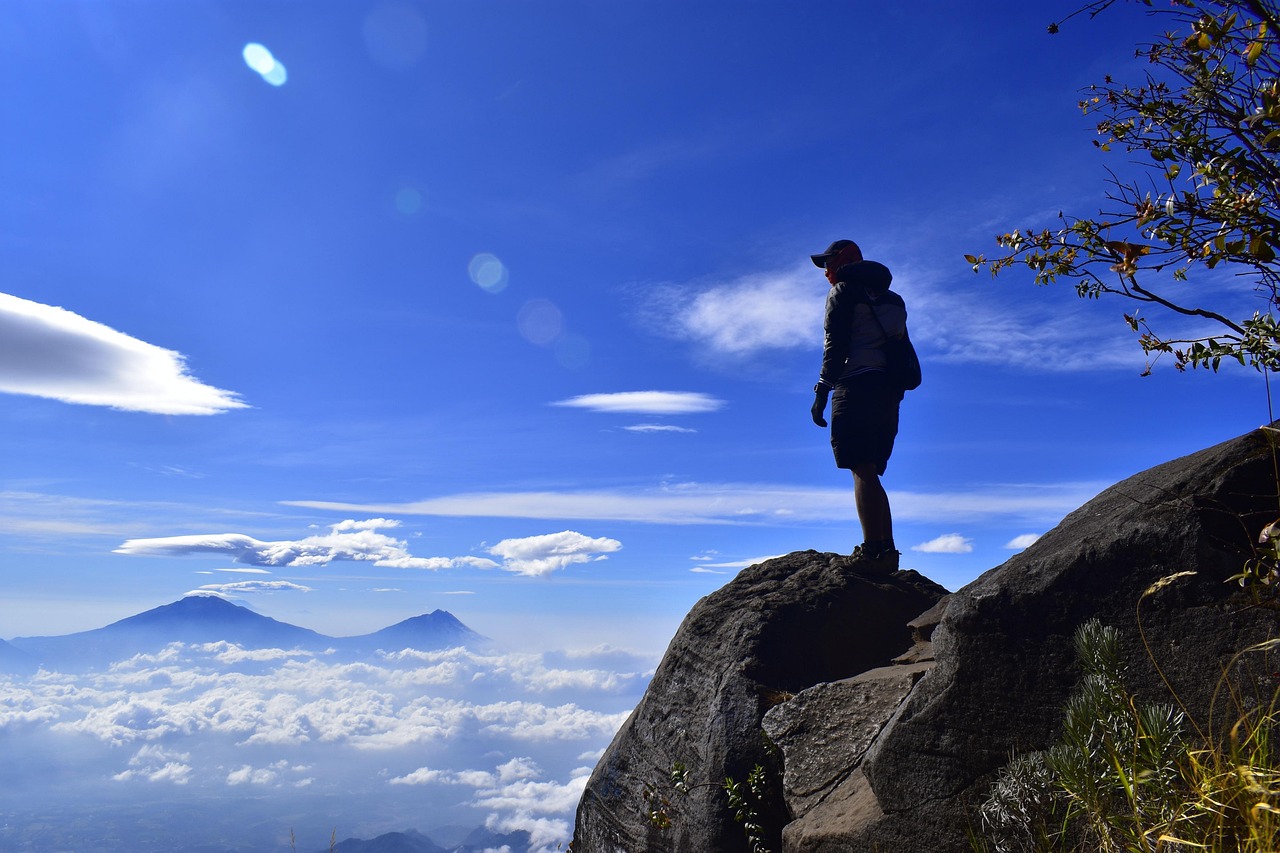 Homme sur un rocher qui observe la vue sur une montagne sur un ciel bleue.